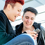 Deux jeunes femmes aux cheveux courts regardent un cellulaire et sourient