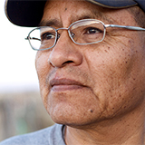 An elderly man in a hat and glasses looking into the distance