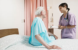 Female clinician stands bedside with an older male patient with a chart in her hand. 