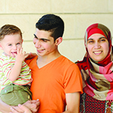 A teenage boy holding a young boy, beside a woman in a head scarf